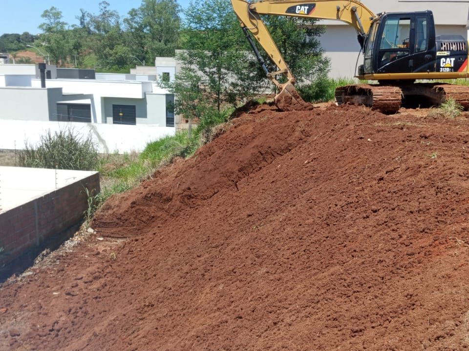 Escavadeira fazendo corte de barranco em lote residencial