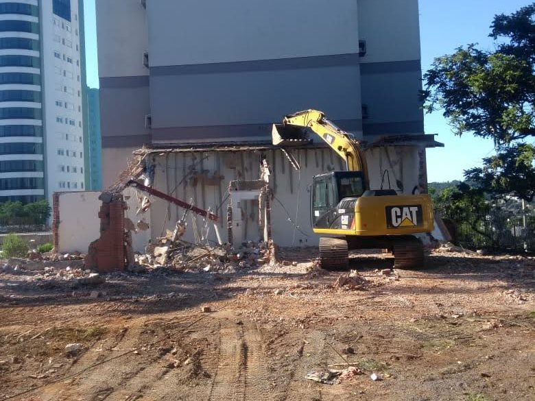 Escavadeira demolindo construção ao lado de prédio