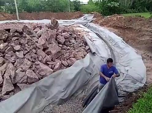 Vala de drenagem com pedras sobre manta sendo executada